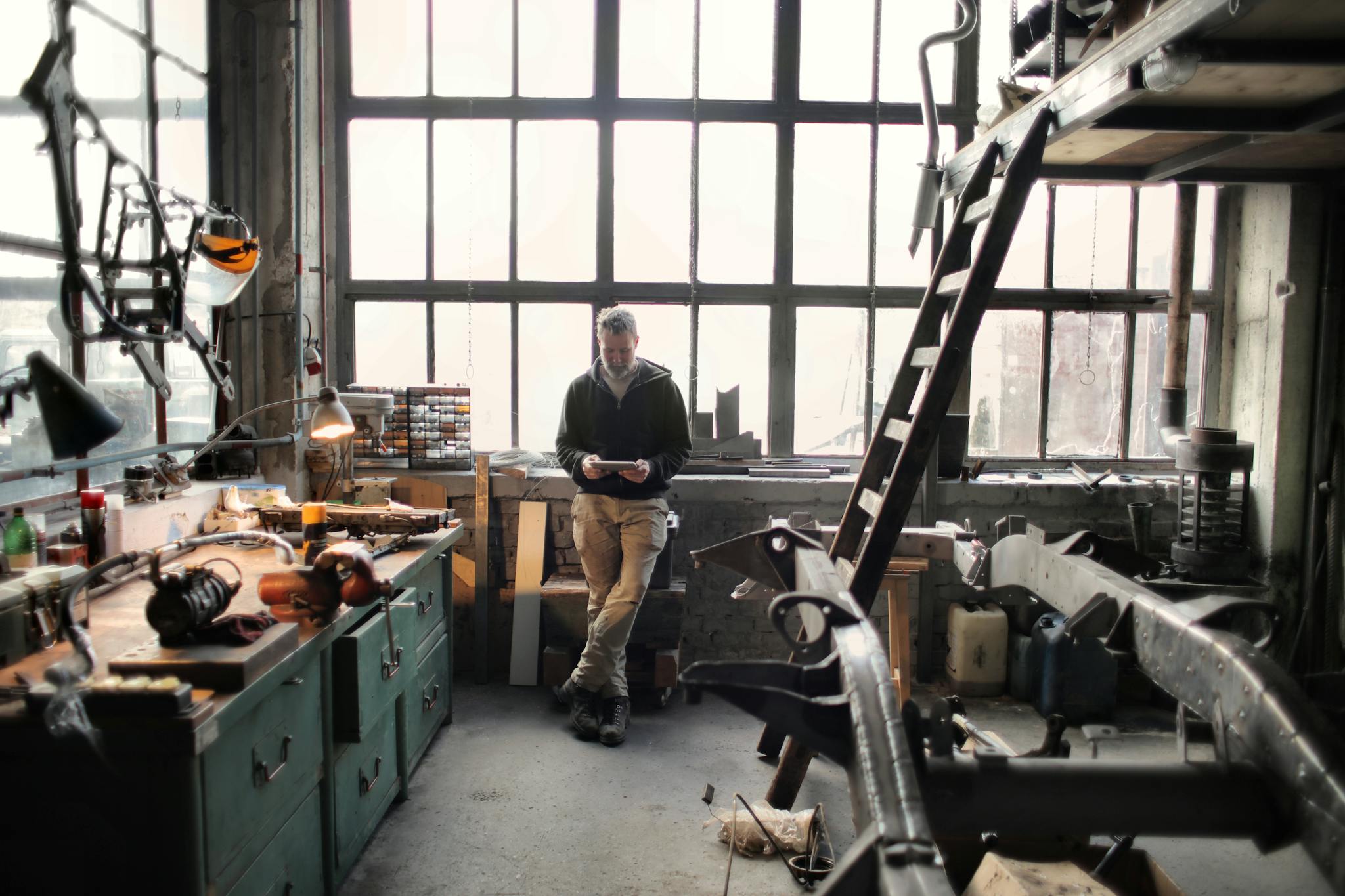 A craftsman stands inside a sunlit workshop, surrounded by tools and machinery.