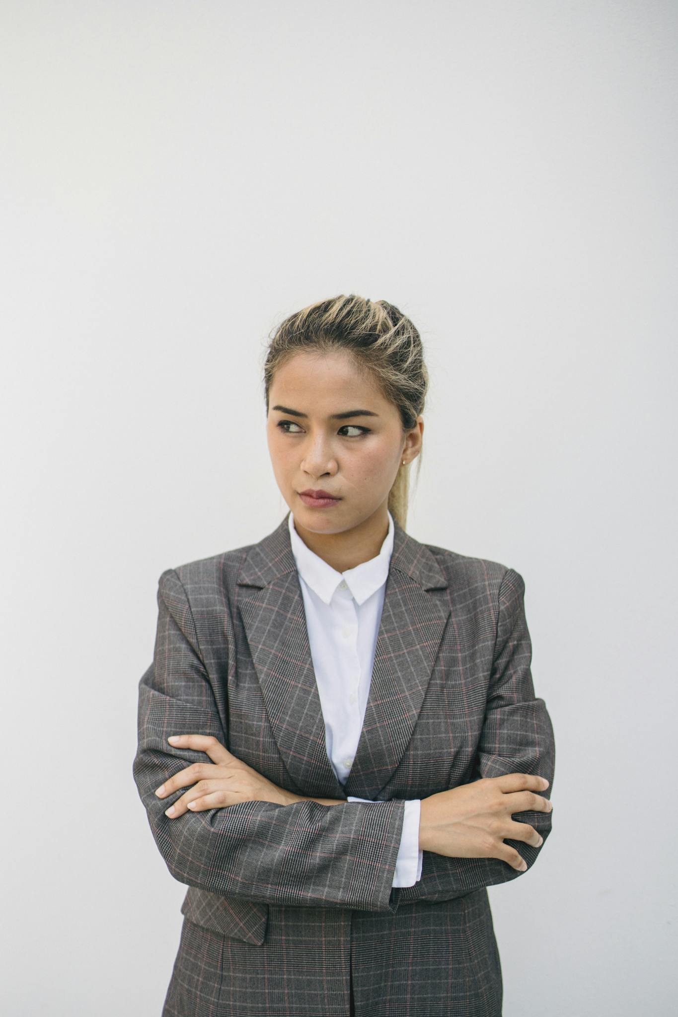 Confident Asian woman poses in a stylish plaid blazer with arms crossed, exuding professionalism.