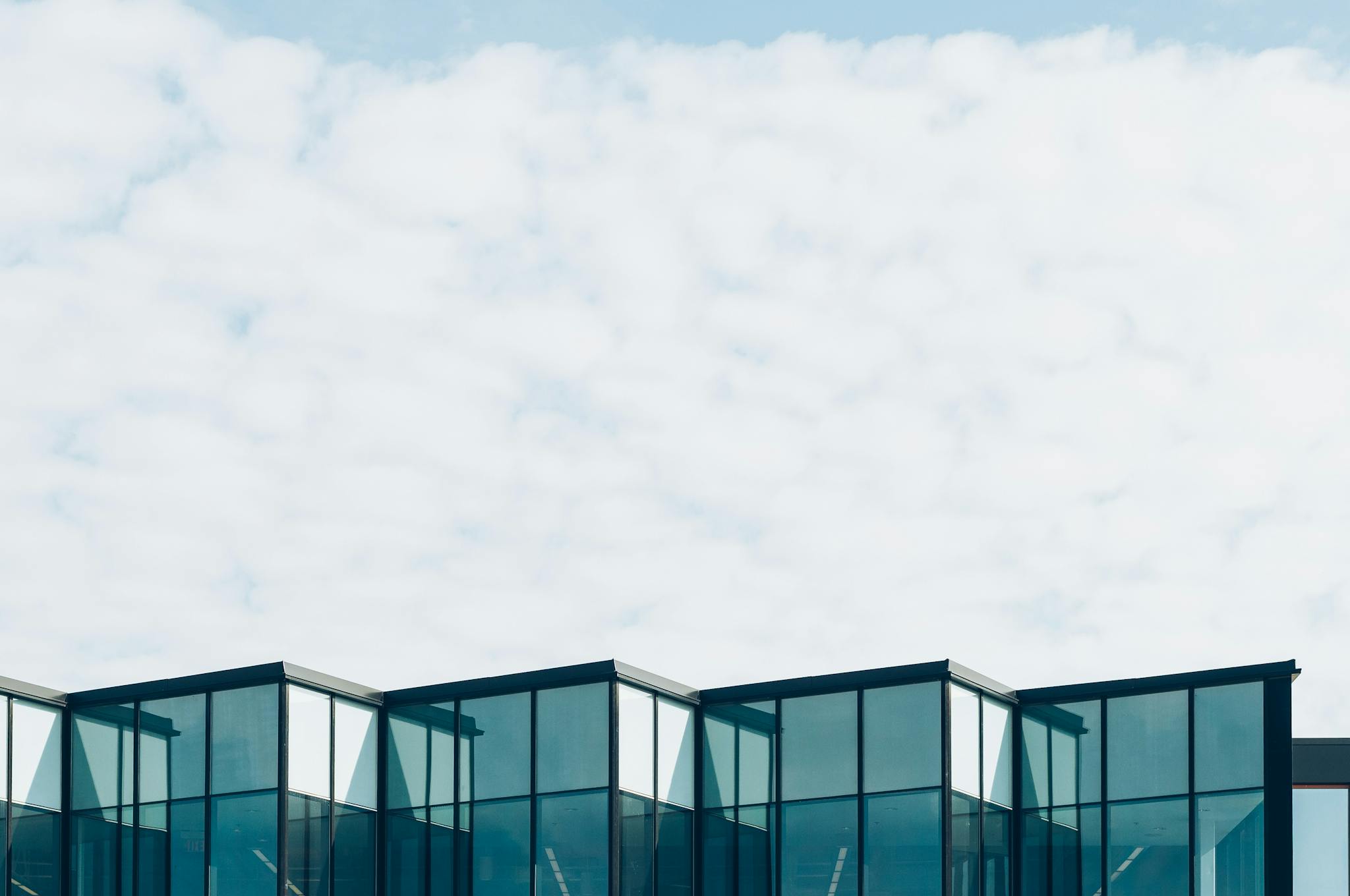 Low angle view of a modern glass building with a cloudy sky background, showcasing contemporary architecture.